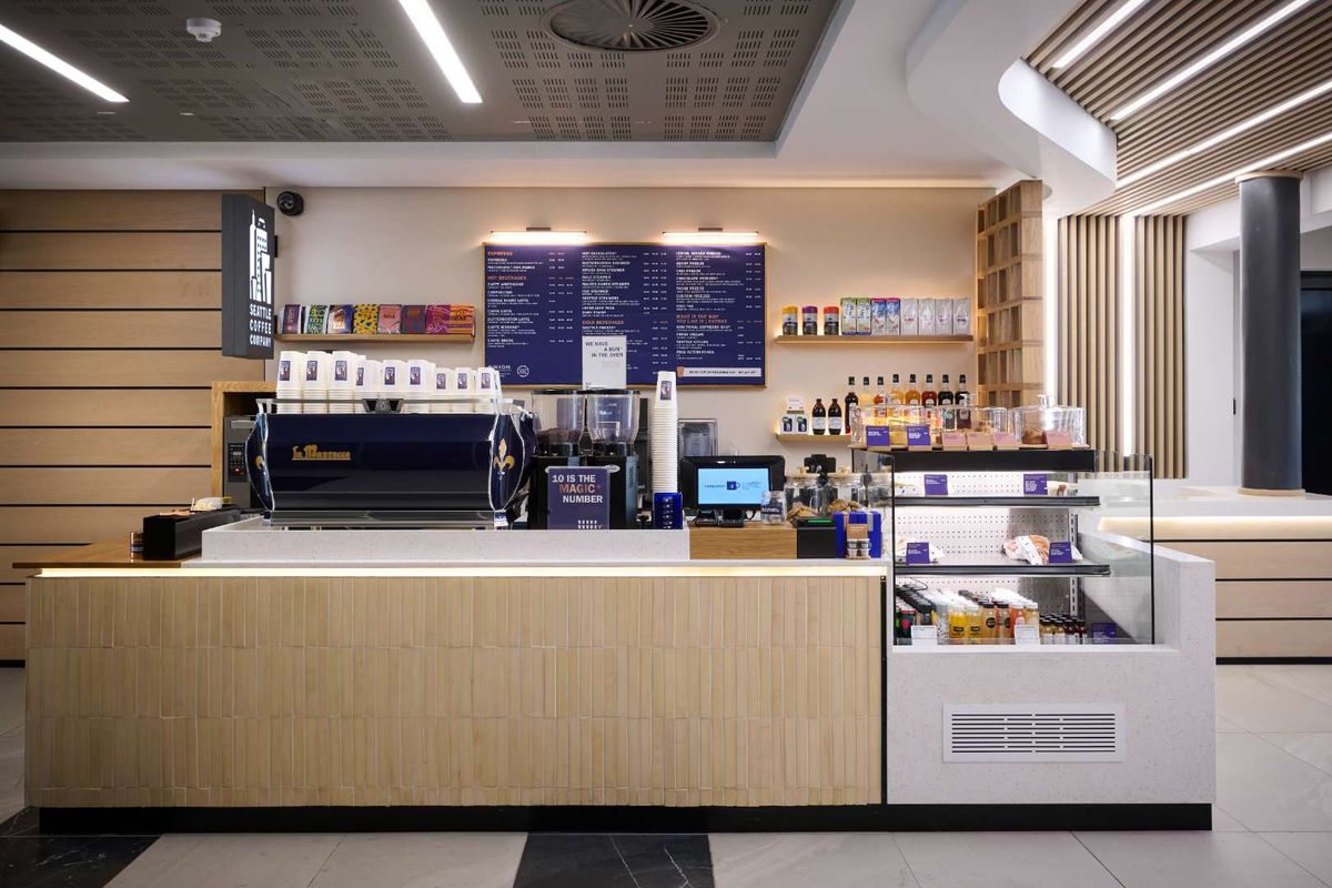 A modern, well-maintained coffee service counter featuring integrated display refrigeration, professional espresso machine, and sleek timber-slat ceiling detailing.