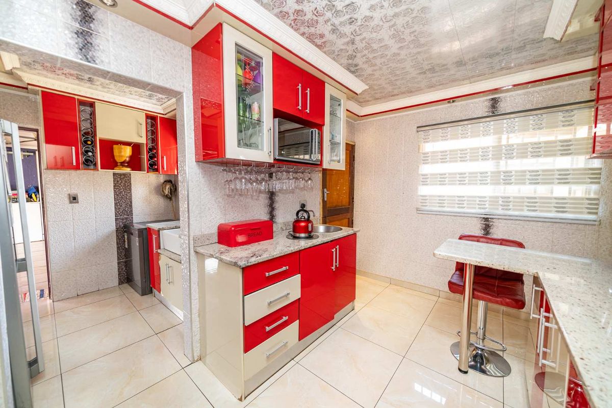 A compact kitchen featuring high-gloss red and cream cabinetry, granite-look countertops, integrated microwave, and tiled flooring with an adjacent scullery area.