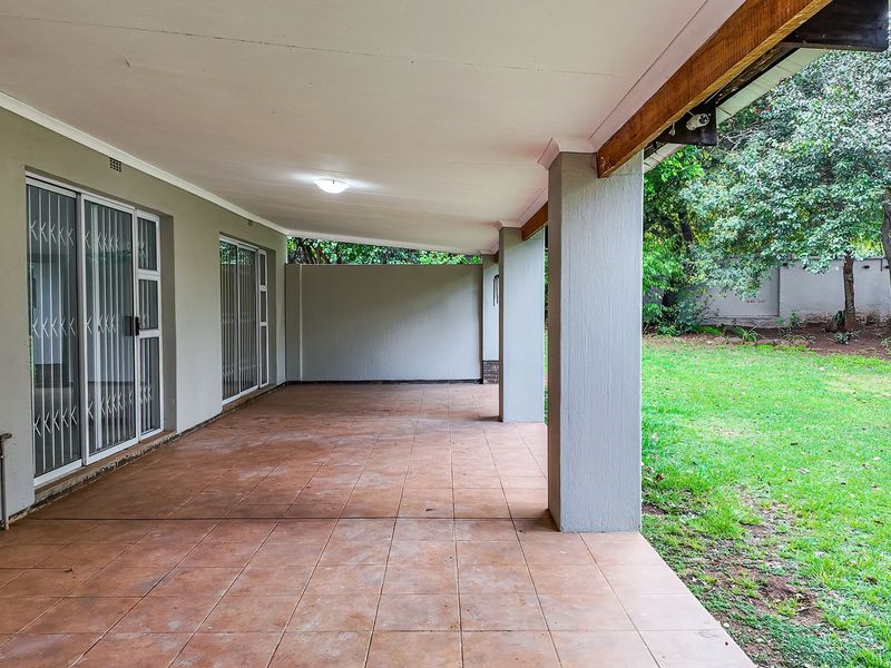 A spacious covered patio featuring tiled flooring and direct access to the garden through sliding glass doors, ideal for outdoor entertaining.