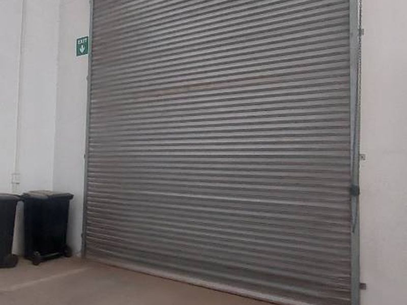 A functional industrial garage space featuring a large metal roller shutter door and durable concrete flooring.