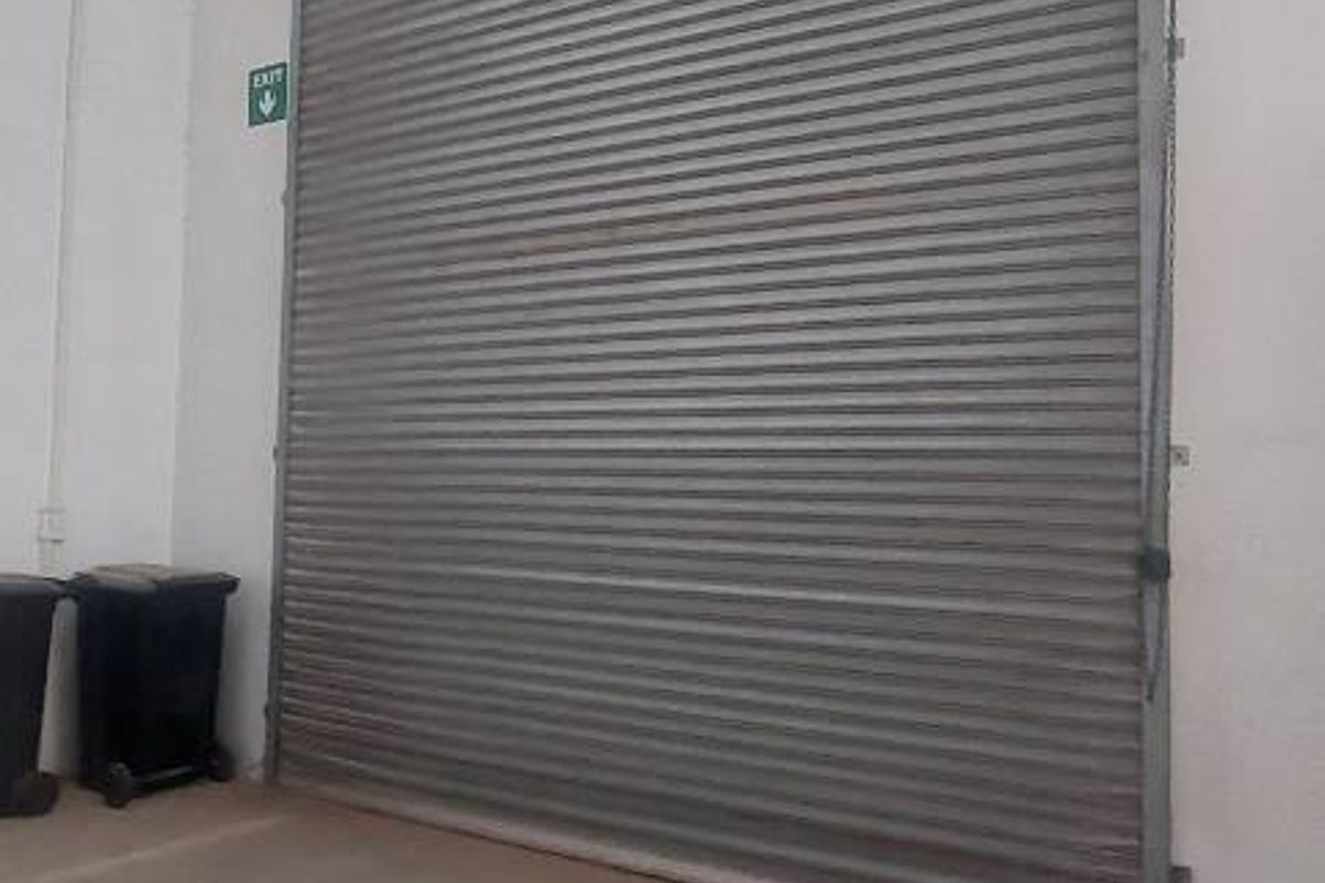 A functional industrial garage space featuring a large metal roller shutter door and durable concrete flooring.