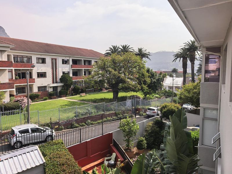 Elevated view overlooking a landscaped communal garden, residential apartment complex, and surrounding neighbourhood with mountain vistas in the distance.