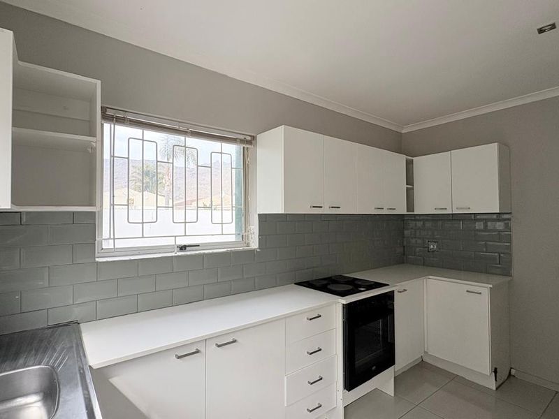 A clean, modern kitchen featuring white cabinetry, grey subway tile backsplash, built-in oven and hob, and a stainless steel sink.
