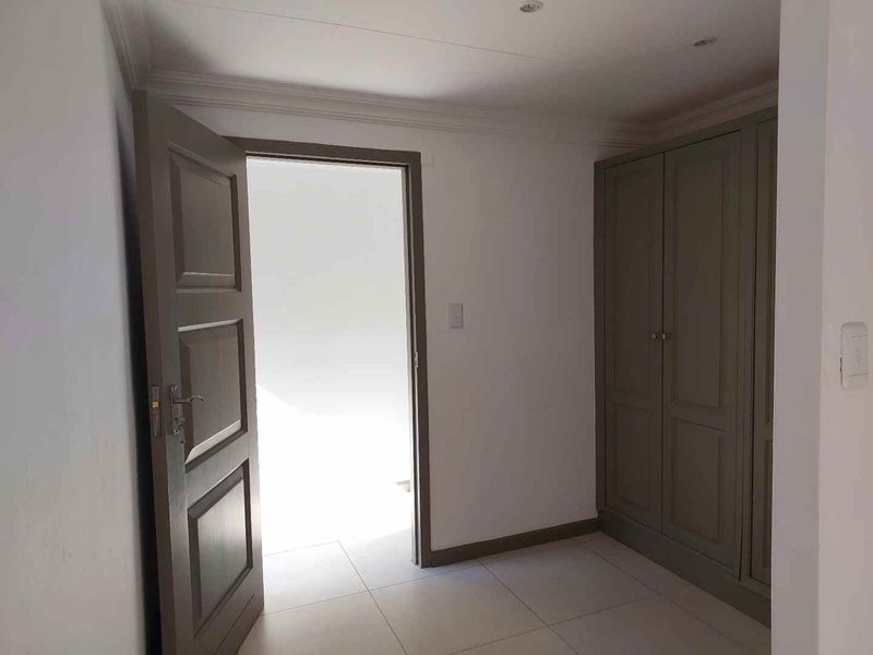 A bedroom featuring built-in cupboards with a neutral finish, tiled flooring, and a doorway leading to an adjacent space.