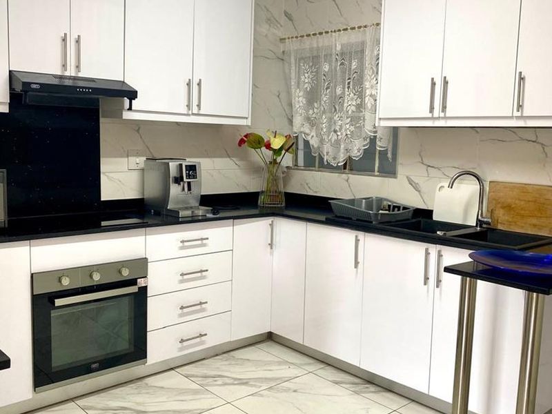 Modern kitchen featuring white cabinetry, contrasting black stone countertops, marble-look tiled flooring, and integrated appliances including an oven and extractor fan.
