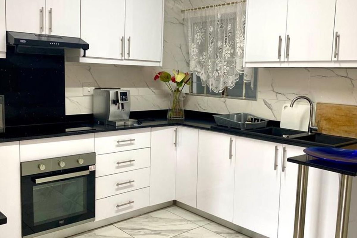 Modern kitchen featuring white cabinetry, contrasting black stone countertops, marble-look tiled flooring, and integrated appliances including an oven and extractor fan.