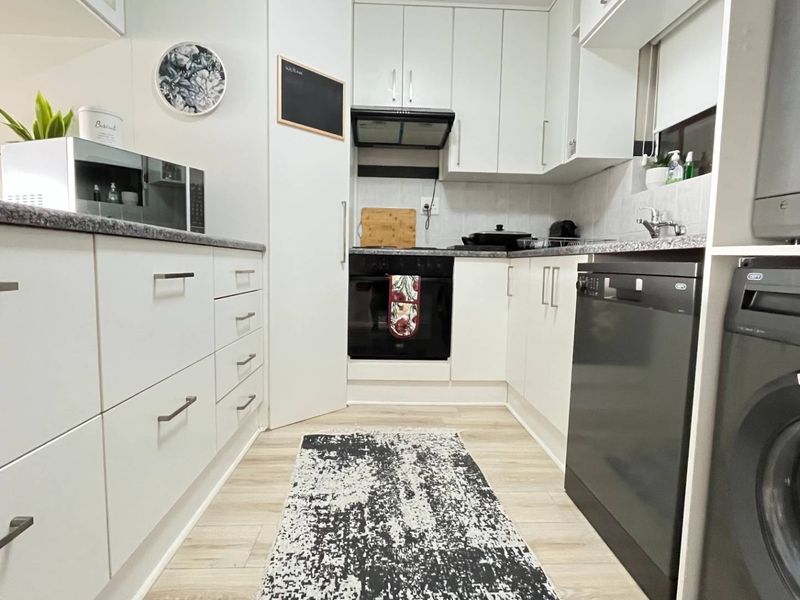 Modern galley-style kitchen featuring white cabinetry, laminate countertops, built-in oven, extractor fan, and integrated dishwasher with light wood-look flooring.