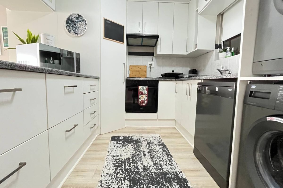 Modern galley-style kitchen featuring white cabinetry, laminate countertops, built-in oven, extractor fan, and integrated dishwasher with light wood-look flooring.
