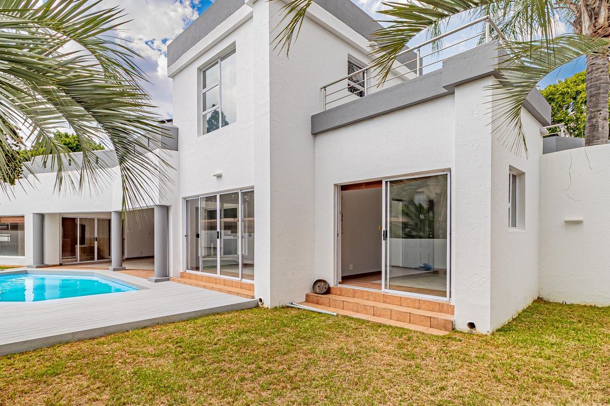 Rear view of a modern two-story home featuring a swimming pool, wooden decking, and a private upper-level balcony with stainless steel railings.