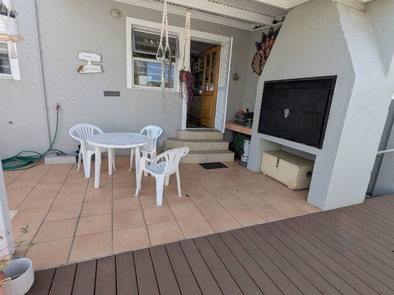 Covered patio area featuring tiled flooring, a built-in braai, and an adjoining timber deck, providing a functional outdoor entertainment space.