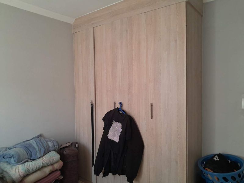 A bedroom featuring a light wood-finish built-in wardrobe with modern handles and ceiling coving.