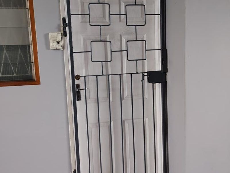 A secure entrance featuring a white panel door protected by a black metal security gate with geometric detailing.
