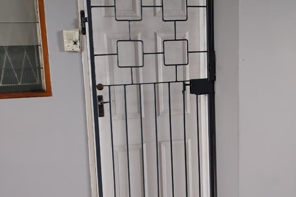 A secure entrance featuring a white panel door protected by a black metal security gate with geometric detailing.