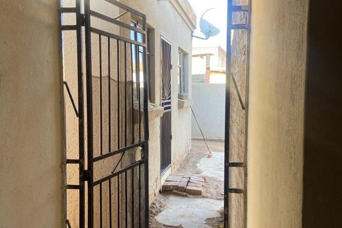 View from an interior doorway looking out towards a side yard area featuring a metal security gate and basic exterior wall finishes.