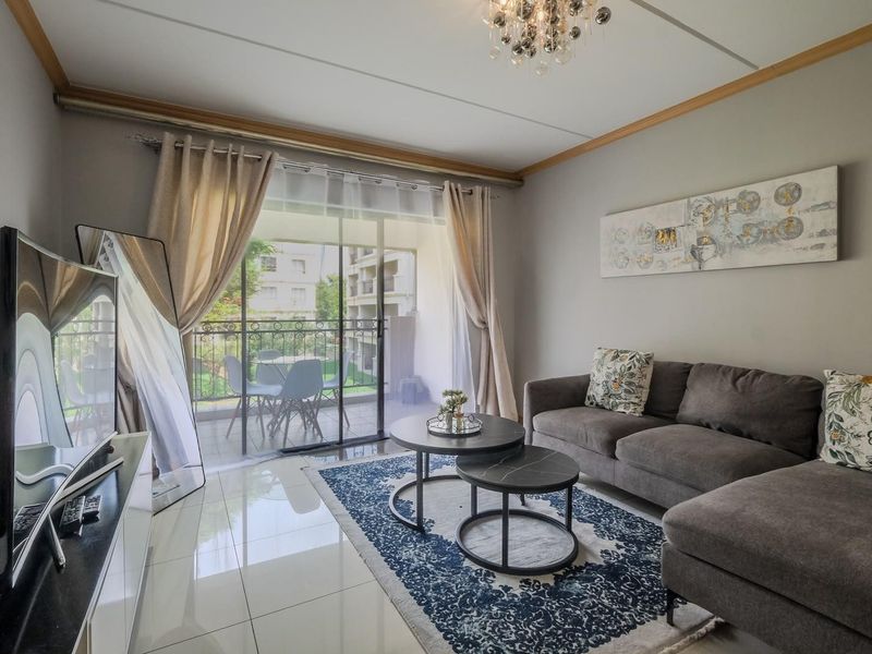 A well-maintained living room featuring polished tile flooring, a modern ceiling light, and a sliding glass door leading to a private balcony.