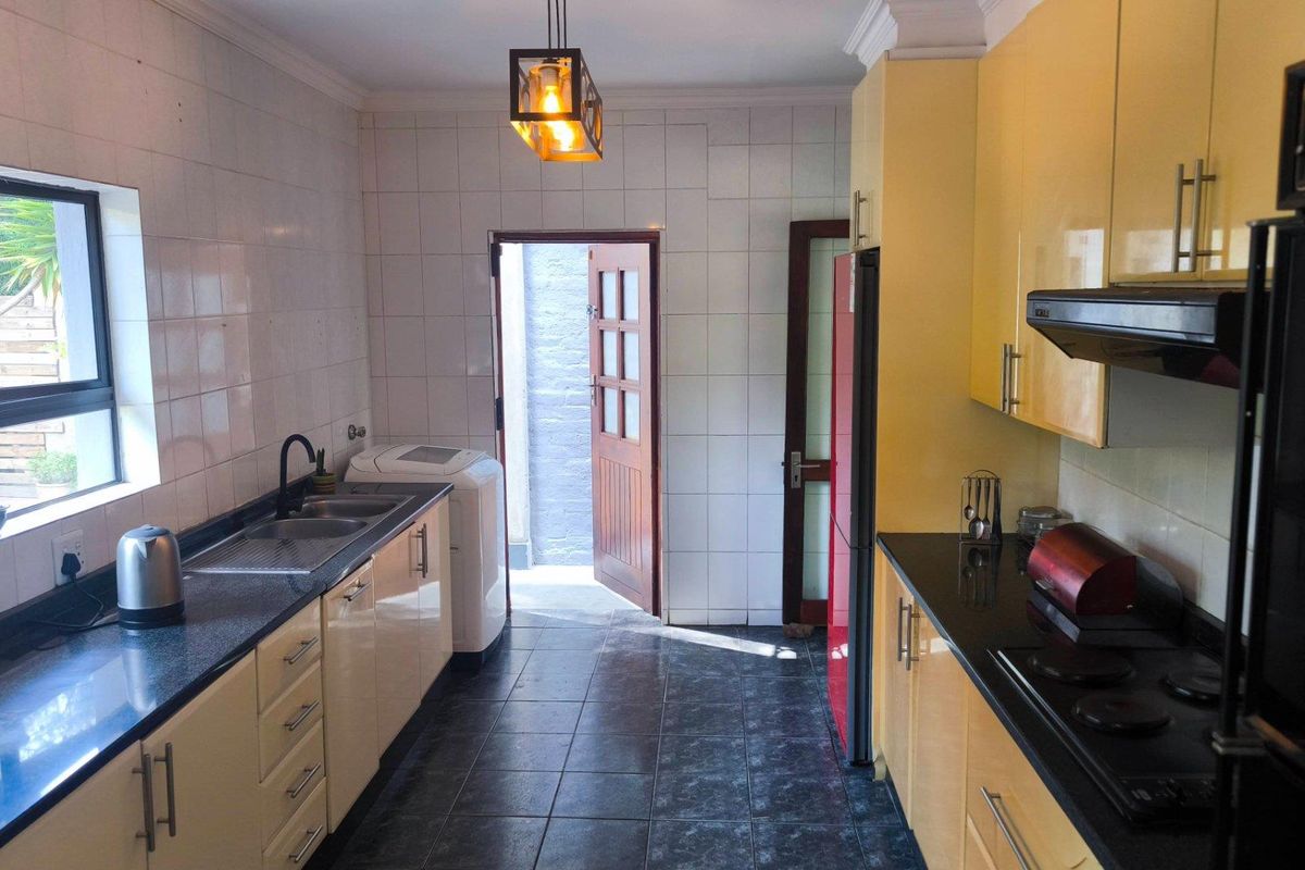 A functional kitchen featuring high-gloss cabinetry, dark granite countertops, a double sink, and a built-in extractor fan with direct access to the rear exterior.