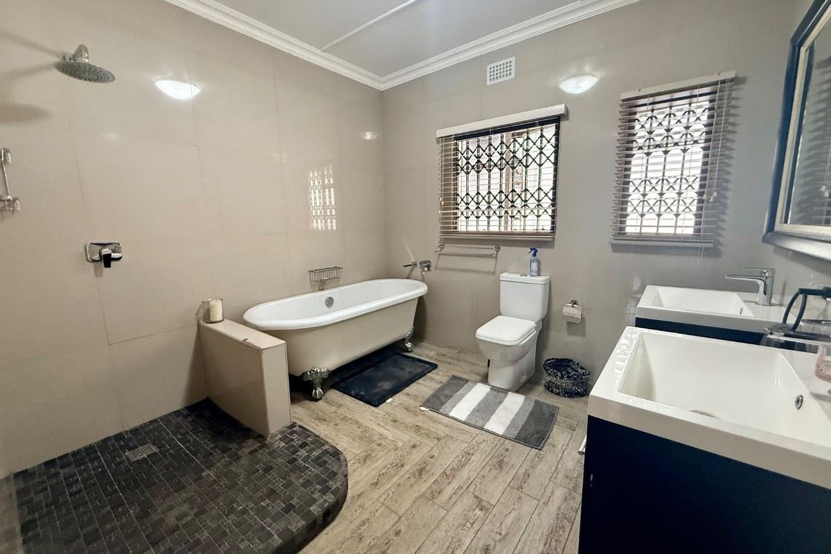 Modern bathroom featuring a freestanding clawfoot bathtub, a walk-in shower with mosaic tiling, dual vanity sinks, and wood-look floor tiles.