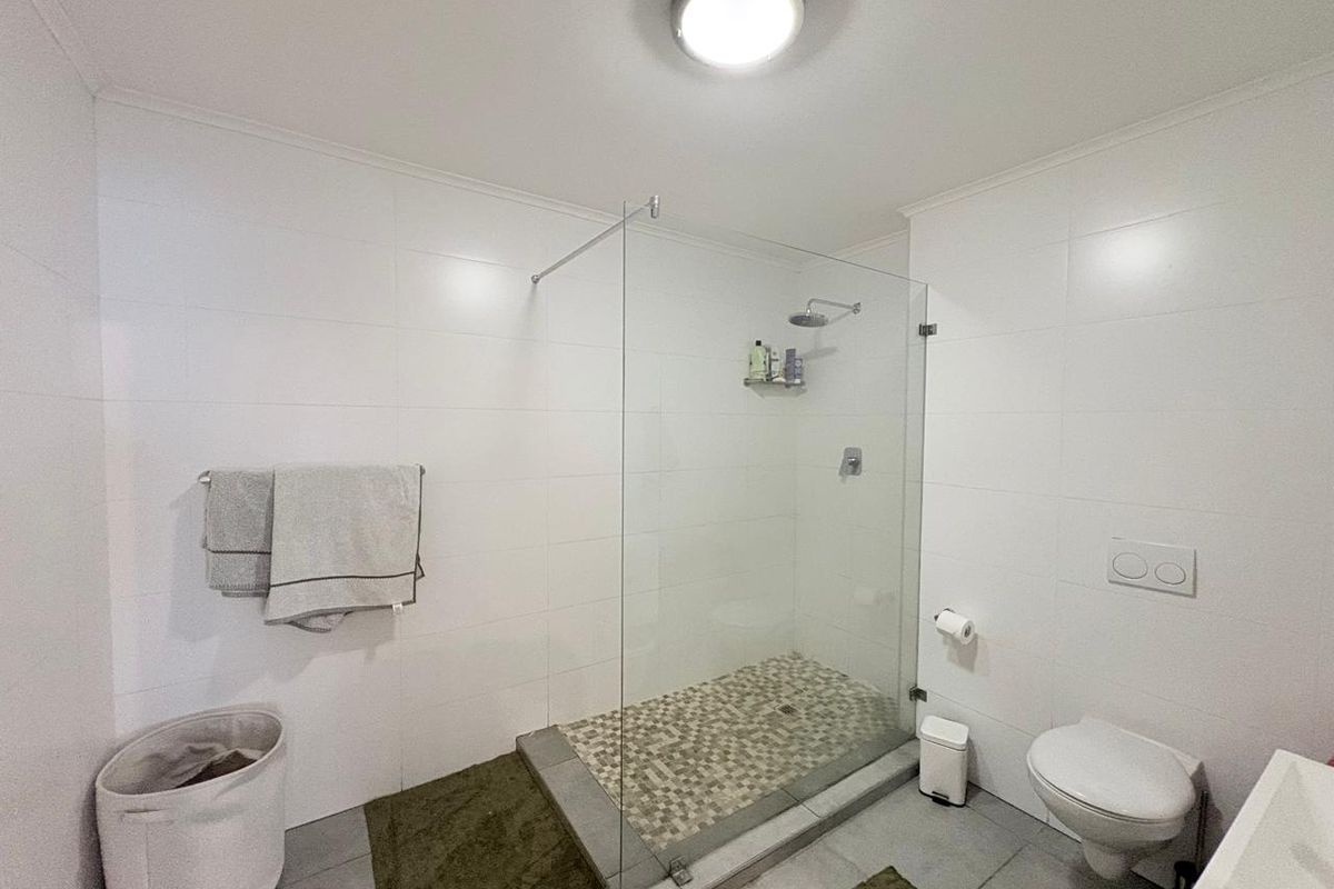 Modern bathroom featuring a walk-in glass shower with mosaic tile flooring, wall-mounted toilet, and clean white wall tiling.