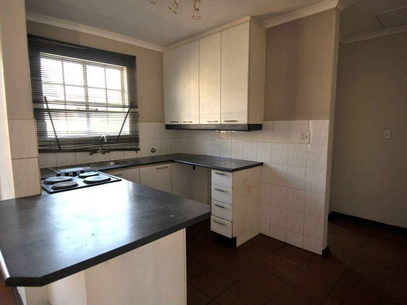 A dated kitchen featuring built-in cabinetry, laminate countertops, an electric hob, and tiled flooring, offering a blank canvas for renovation.