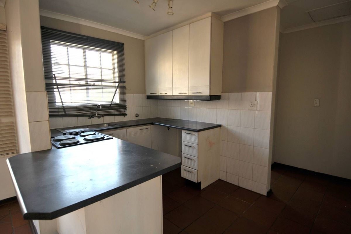 A dated kitchen featuring built-in cabinetry, laminate countertops, an electric hob, and tiled flooring, offering a blank canvas for renovation.