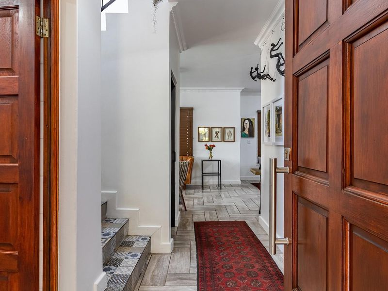 Welcoming entrance hall featuring a solid timber front door, decorative tiled staircase, and neutral tiled flooring leading into the main living area.