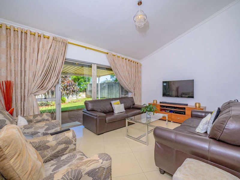A bright living room featuring tiled flooring, a large sliding glass door providing access to the garden, and elegant cove cornicing.