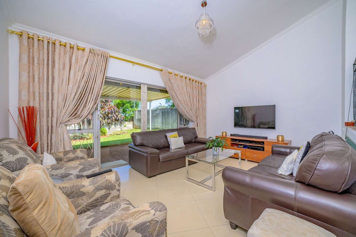 A bright living room featuring tiled flooring, a large sliding glass door providing access to the garden, and elegant cove cornicing.