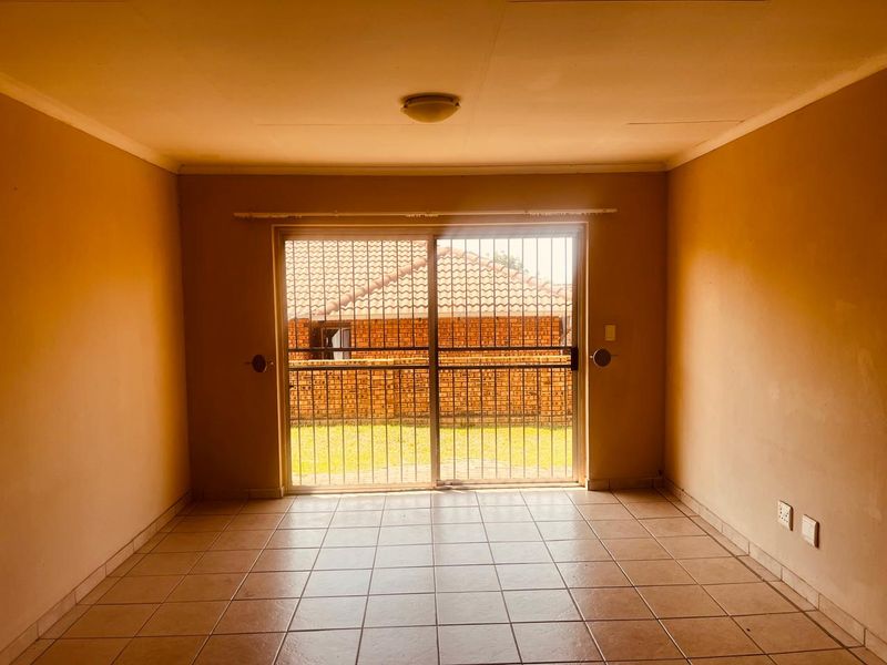 An empty living room featuring tiled flooring and a sliding glass door with a security gate, providing access to the rear exterior area.