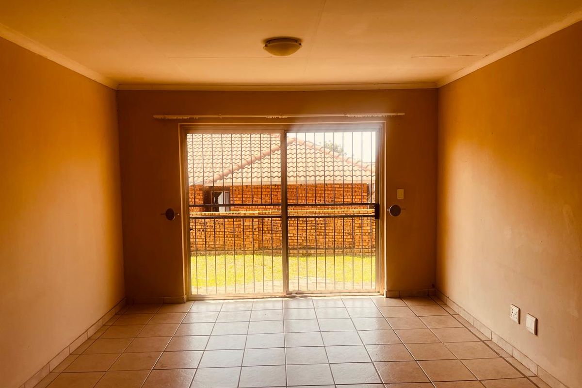 An empty living room featuring tiled flooring and a sliding glass door with a security gate, providing access to the rear exterior area.