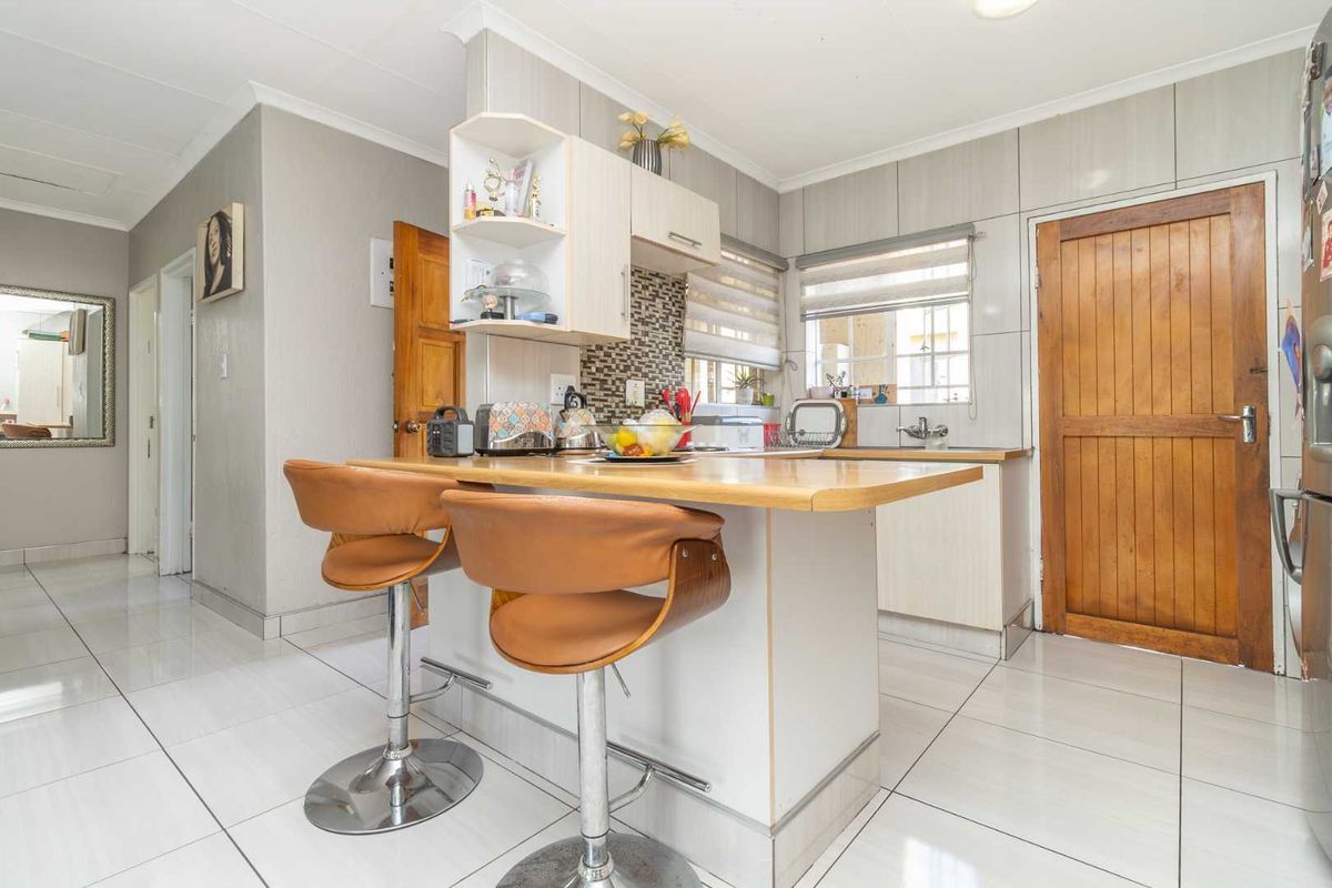 A functional kitchen featuring a breakfast bar, mosaic tile backsplash, tiled flooring, and wooden door access.
