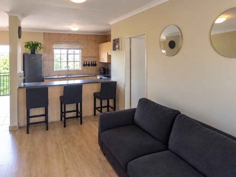 Open-plan living area featuring a functional kitchen with breakfast bar, laminate flooring, and direct access to an outdoor balcony.
