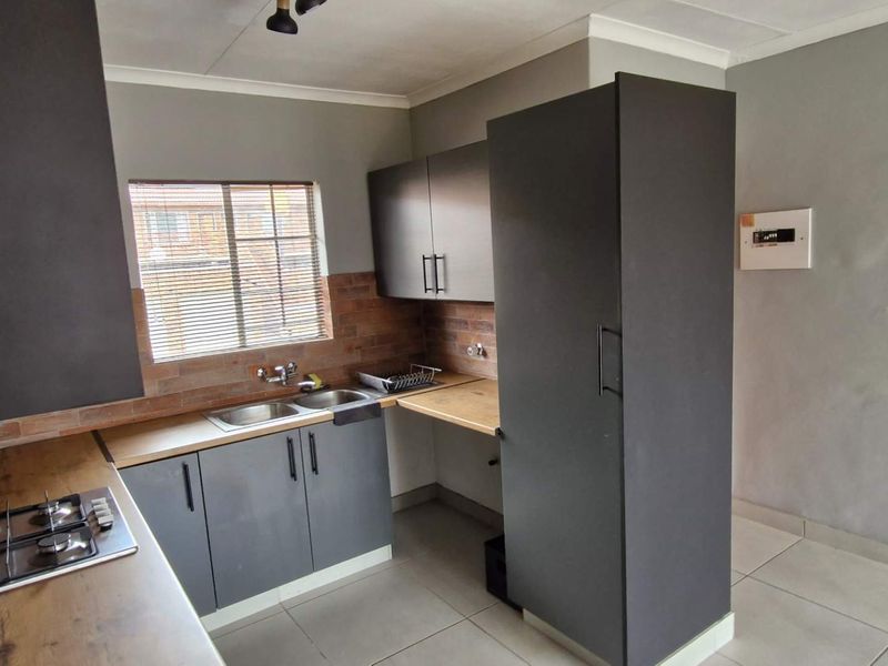A modern kitchen featuring dark cabinetry, a gas hob, double sink, and brick-style backsplash, offering a functional and contemporary workspace.