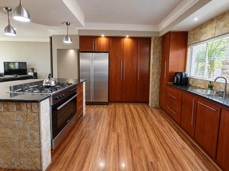 Modern kitchen featuring warm wood cabinetry, granite countertops, stone-clad island with gas stove, and high-quality stainless steel appliances.