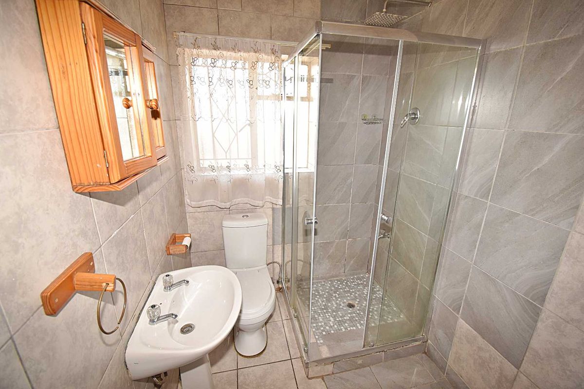 A compact bathroom featuring a glass-enclosed shower, pedestal basin, and toilet, finished with neutral wall and floor tiling.