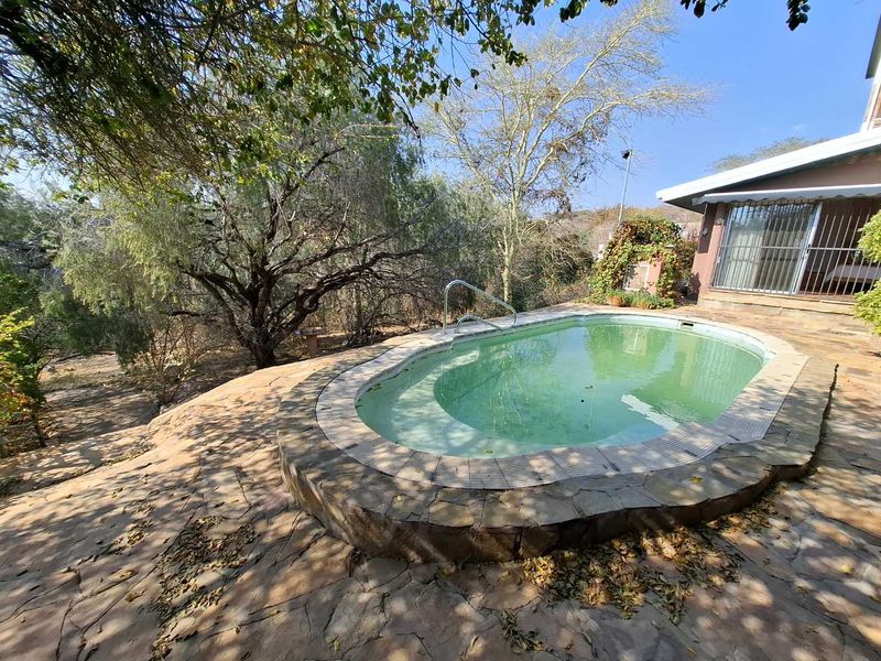 Outdoor pool area featuring a raised stone-paved surround, pool handrail, and direct access to the home via sliding glass doors.