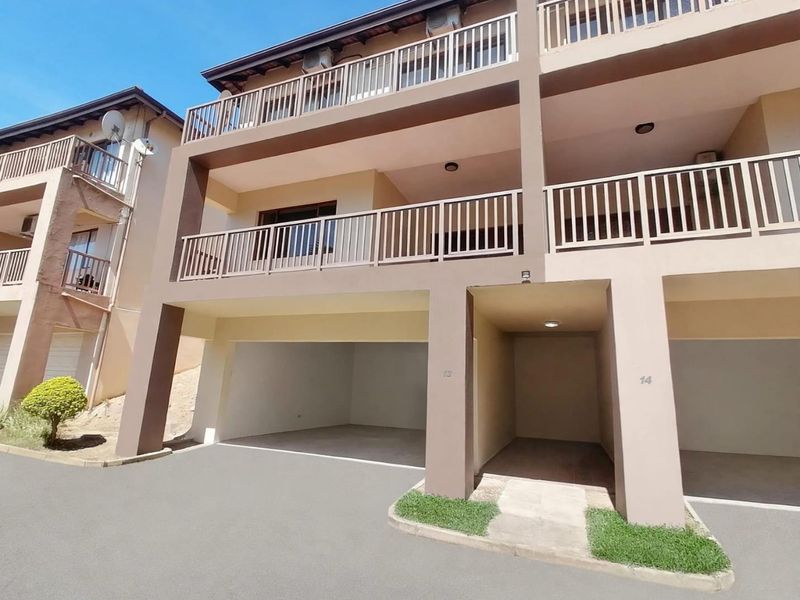 Front elevation of a multi-story townhouse complex featuring covered ground-level parking bays and upper-level balconies with metal railings.