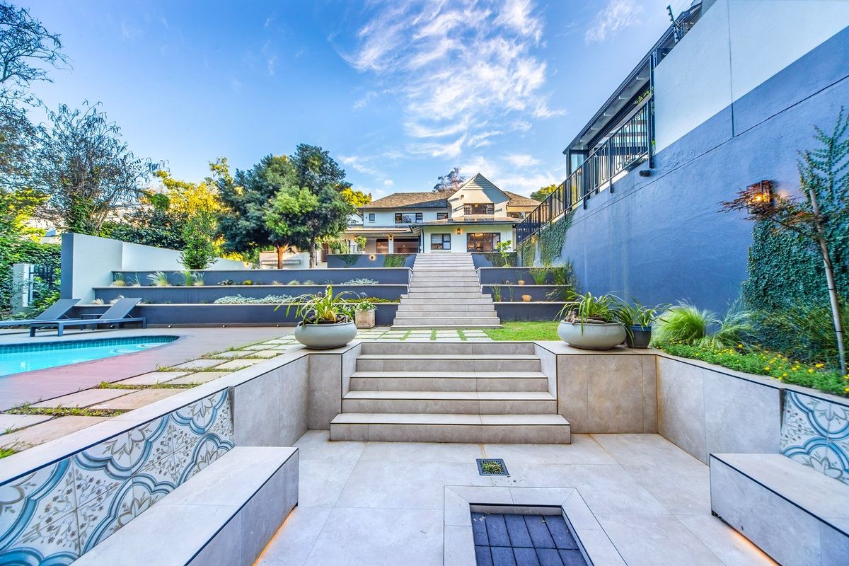A beautifully landscaped rear garden featuring a swimming pool, tiered stone retaining walls, central staircase, and a modern tiled patio with built-in seating.