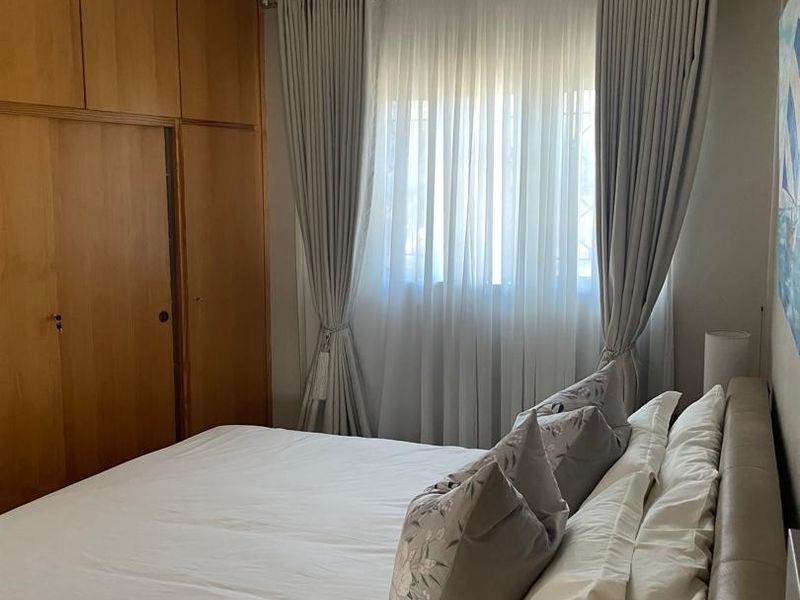 A bedroom featuring built-in wooden cupboards and a window with fitted curtains.