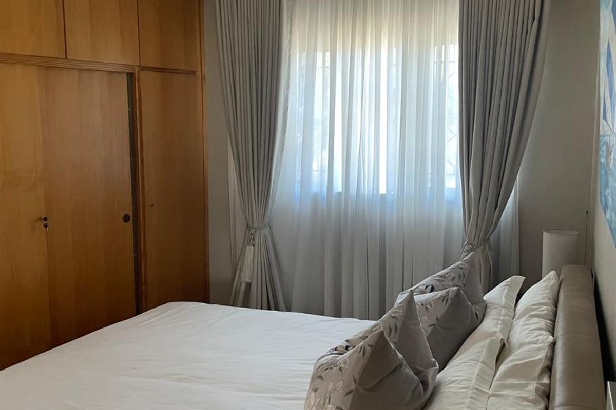 A bedroom featuring built-in wooden cupboards and a window with fitted curtains.