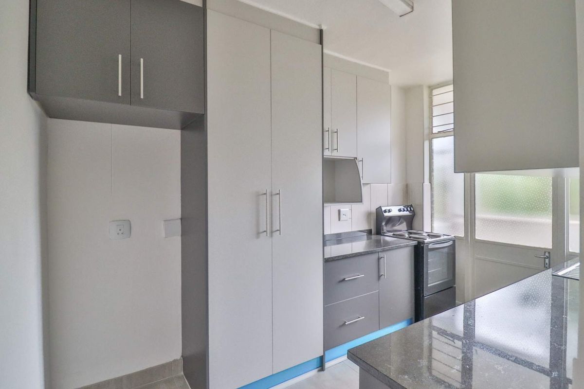 A clean, modern kitchen featuring neutral-toned built-in cabinetry, stone countertops, and a freestanding stove, offering a functional and well-maintained cooking space.