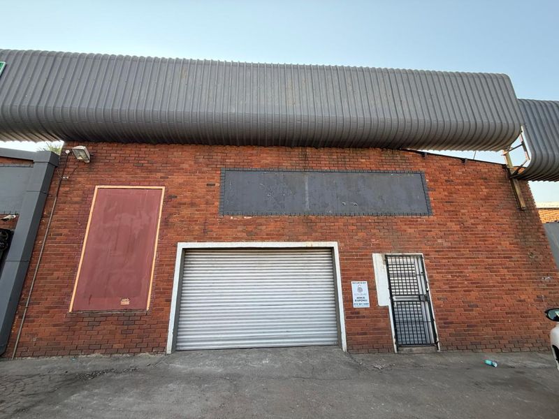 Front elevation of a commercial industrial unit featuring exposed brickwork, a secure roller shutter door, and a prominent metal roof canopy.
