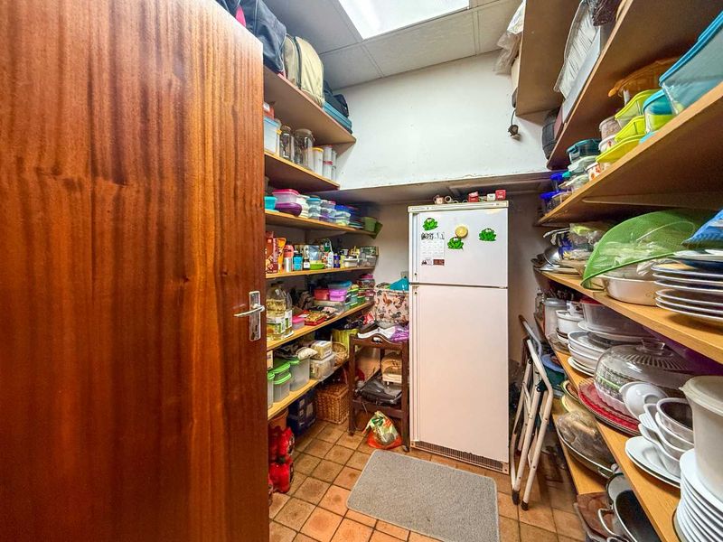 A functional scullery or pantry area featuring extensive built-in shelving and tiled flooring, providing ample storage space for kitchen essentials.