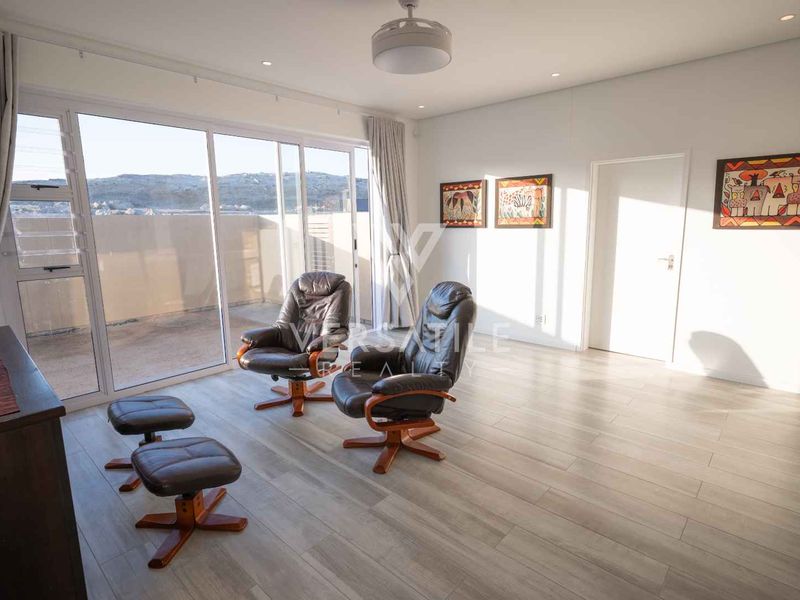 A bright living room featuring modern laminate flooring, recessed lighting, and large sliding glass doors that provide access to an outdoor balcony area.