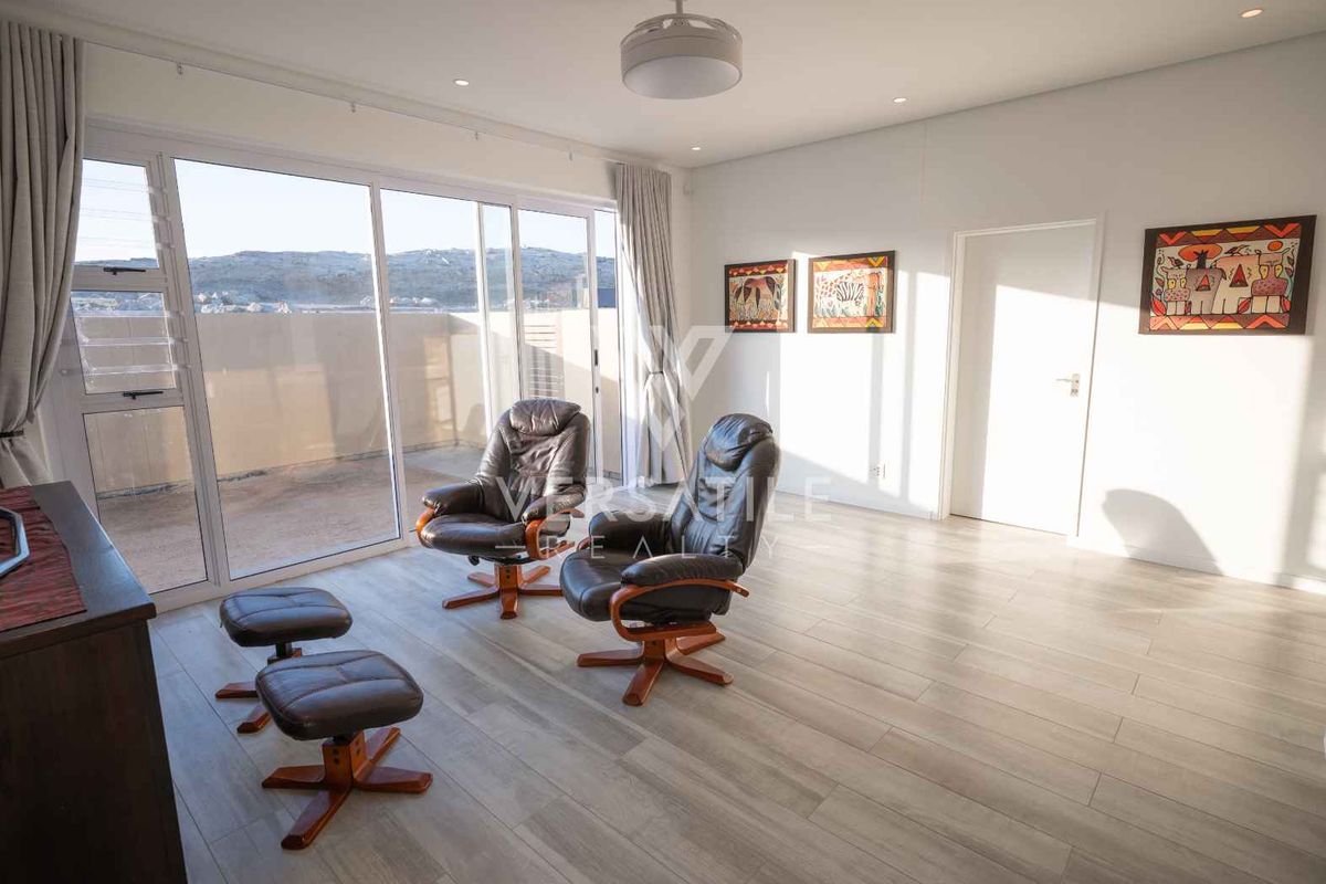 A bright living room featuring modern laminate flooring, recessed lighting, and large sliding glass doors that provide access to an outdoor balcony area.