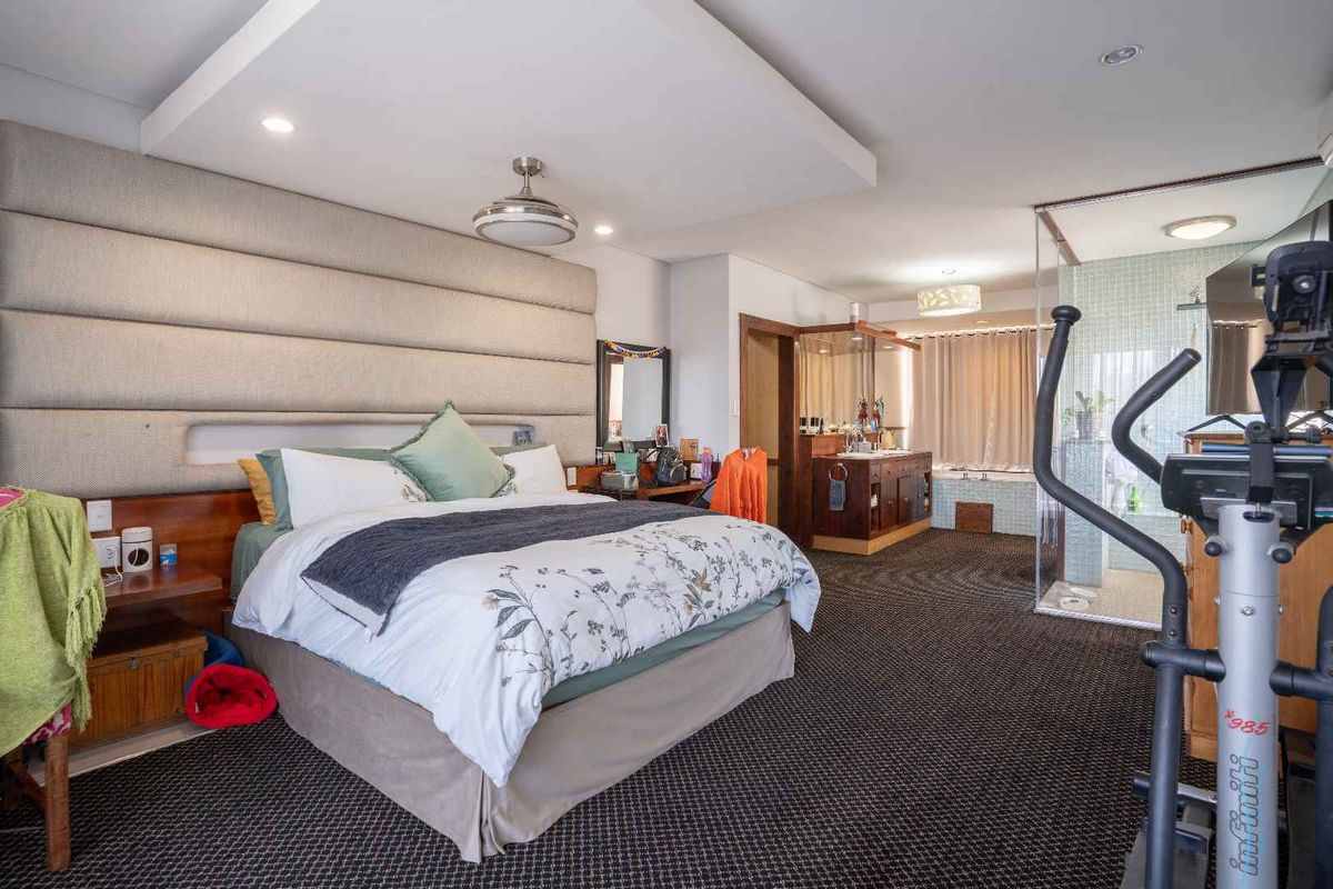 Spacious bedroom featuring a large upholstered headboard wall, recessed ceiling lighting, and an open-plan en-suite bathroom with a glass shower and built-in vanity.