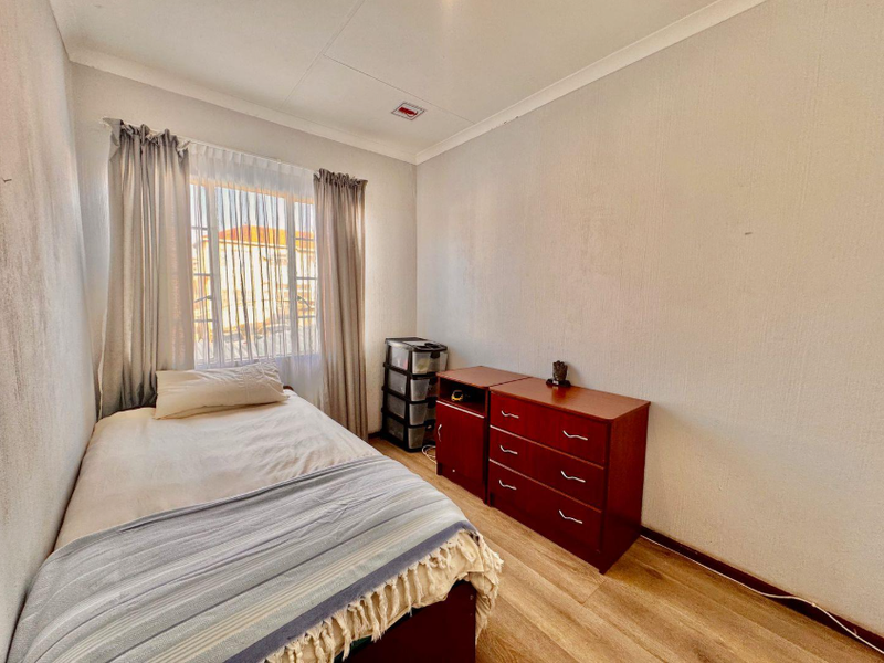 A functional bedroom featuring laminate flooring, a window with curtains, and a standard ceiling with a visible crack in the panel.