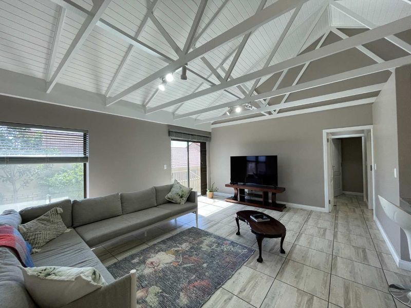 Spacious living room featuring a high vaulted ceiling with exposed white timber trusses, tiled flooring, and large sliding glass doors providing natural light.