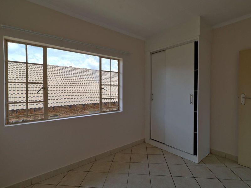 A bright, empty bedroom featuring tiled flooring and a built-in sliding door wardrobe, offering a clean and neutral space ready for personalization.