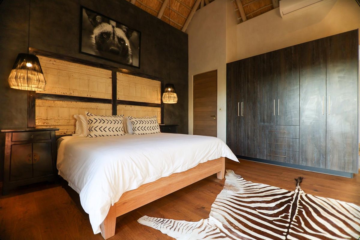A well-appointed bedroom featuring a high thatched ceiling, dark wood built-in cabinetry, and warm timber flooring.