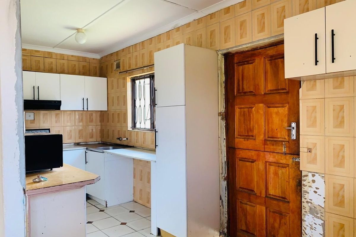 A functional kitchen space featuring built-in cabinetry, tiled splashbacks, and tiled flooring, currently requiring cosmetic updates and finishing touches to the wall surfaces.